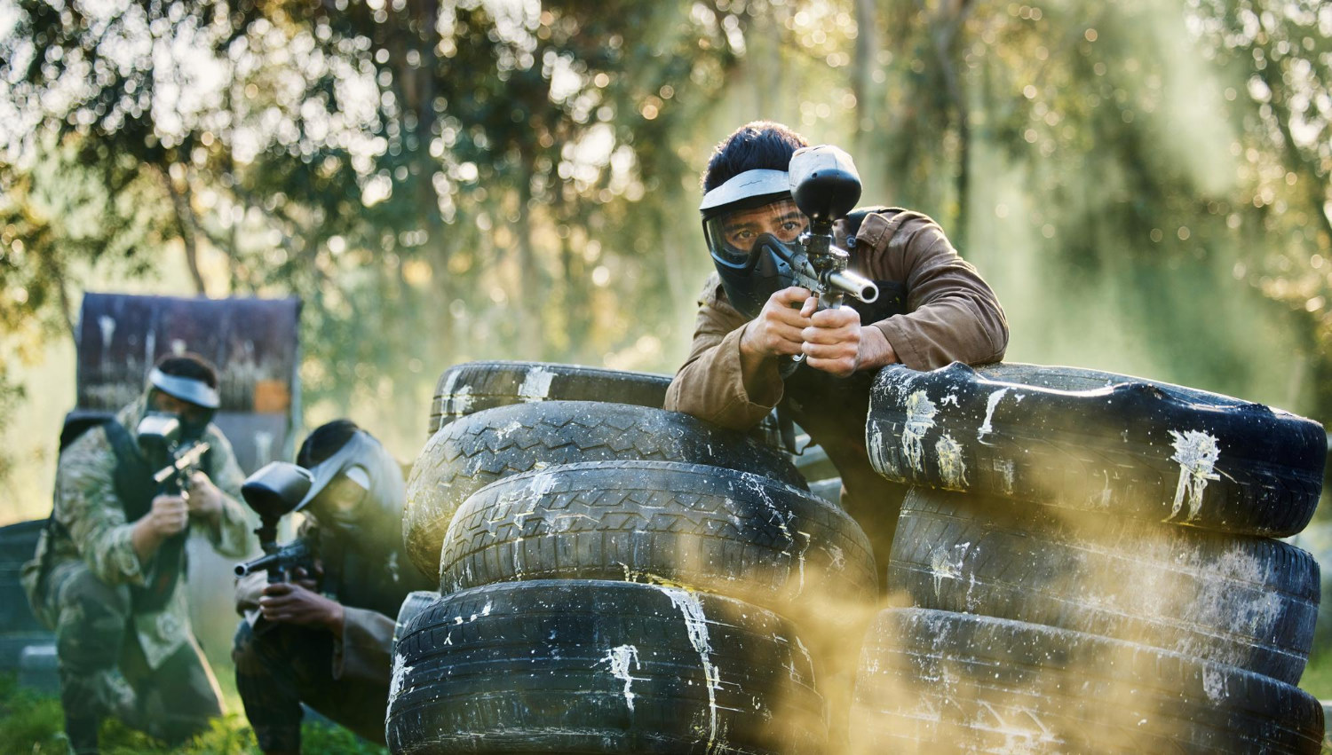 Alguns jogadores de paintball a protegerem-se atrás de pneus.