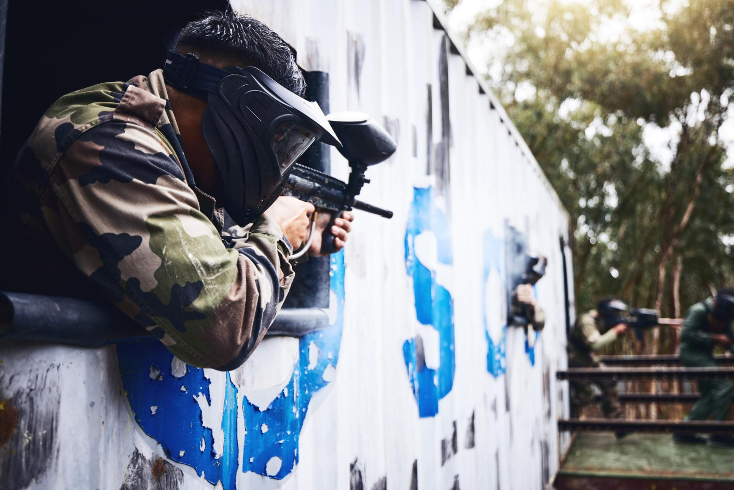 Um jogador de paintball a disparar de uma janela para outro jogador.